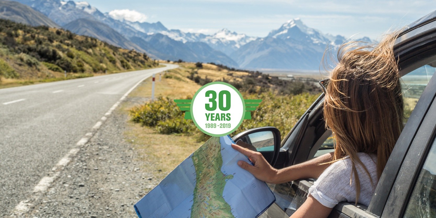 Woman looks out to the road, holding a map in the passenger seat of a parked rental car.