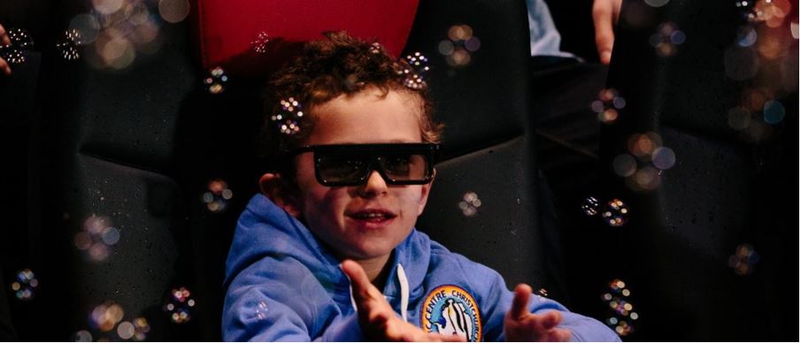a kid with 3D glasses playing with bubbles at the 4D theater.